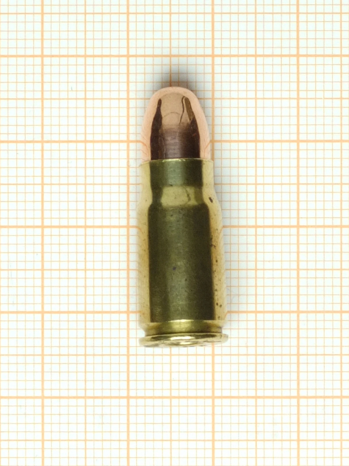 A bottleneck brass pistol cartridge with a rounded copper-jacketed bullet, photographed on graph paper.