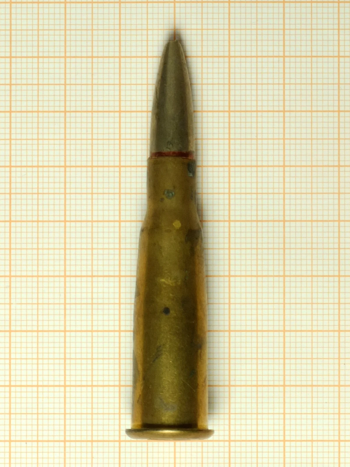 A single 8×50mmR Lebel cartridge lying on graph paper, brass case with a pronounced double taper and a red-banded spitzer bullet