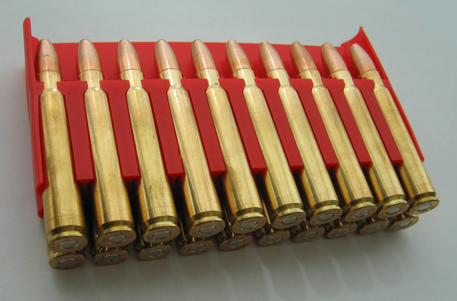 A row of brass rifle cartridges with round-nosed bullets, packed in a red box