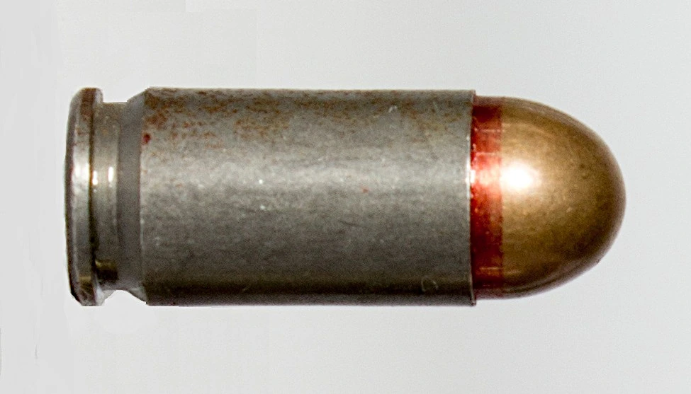 A 9×18mm Makarov cartridge lying on its side, close up, with a steel case and a red sealant ring at the case mouth.