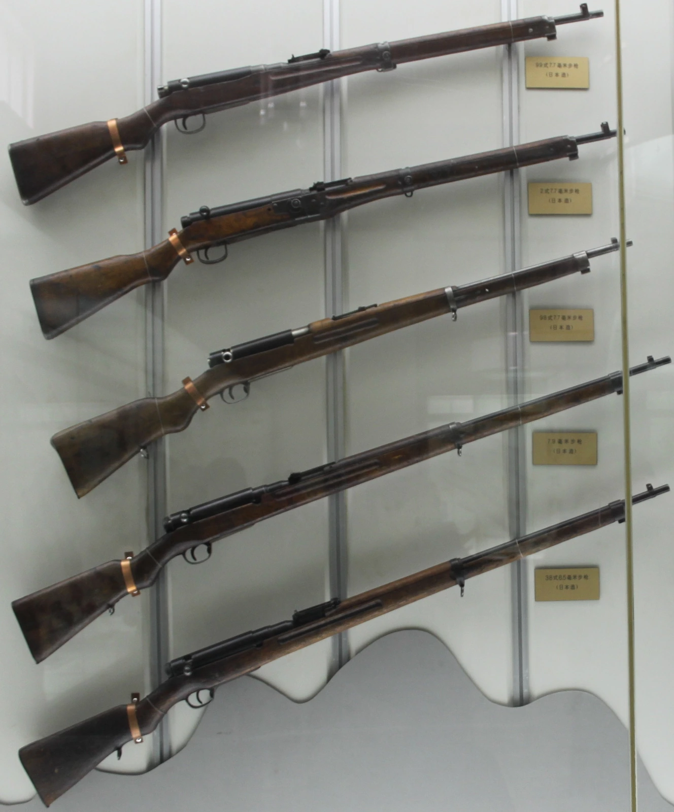 Four Arisaka rifles racked upright behind glass, wood stocks and long barrels visible