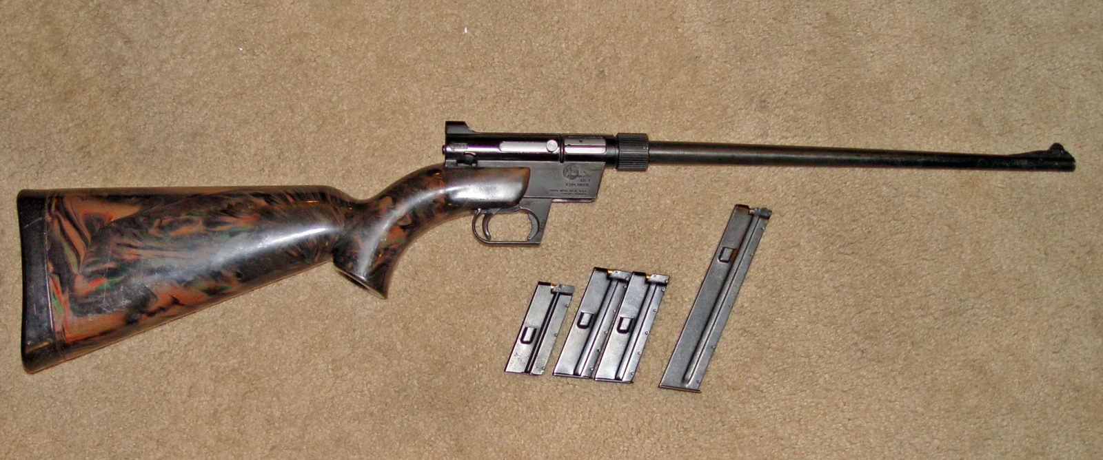 A takedown .22 rifle with wooden-look stock laid on a surface beside three detachable box magazines