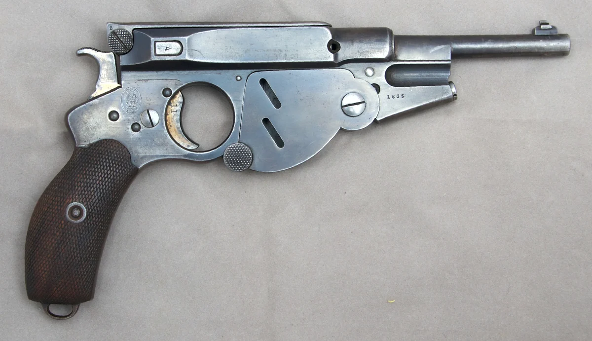 The right side of the same pistol, showing a fan-shaped hinged cover over the loading port and a round cutout in the frame.