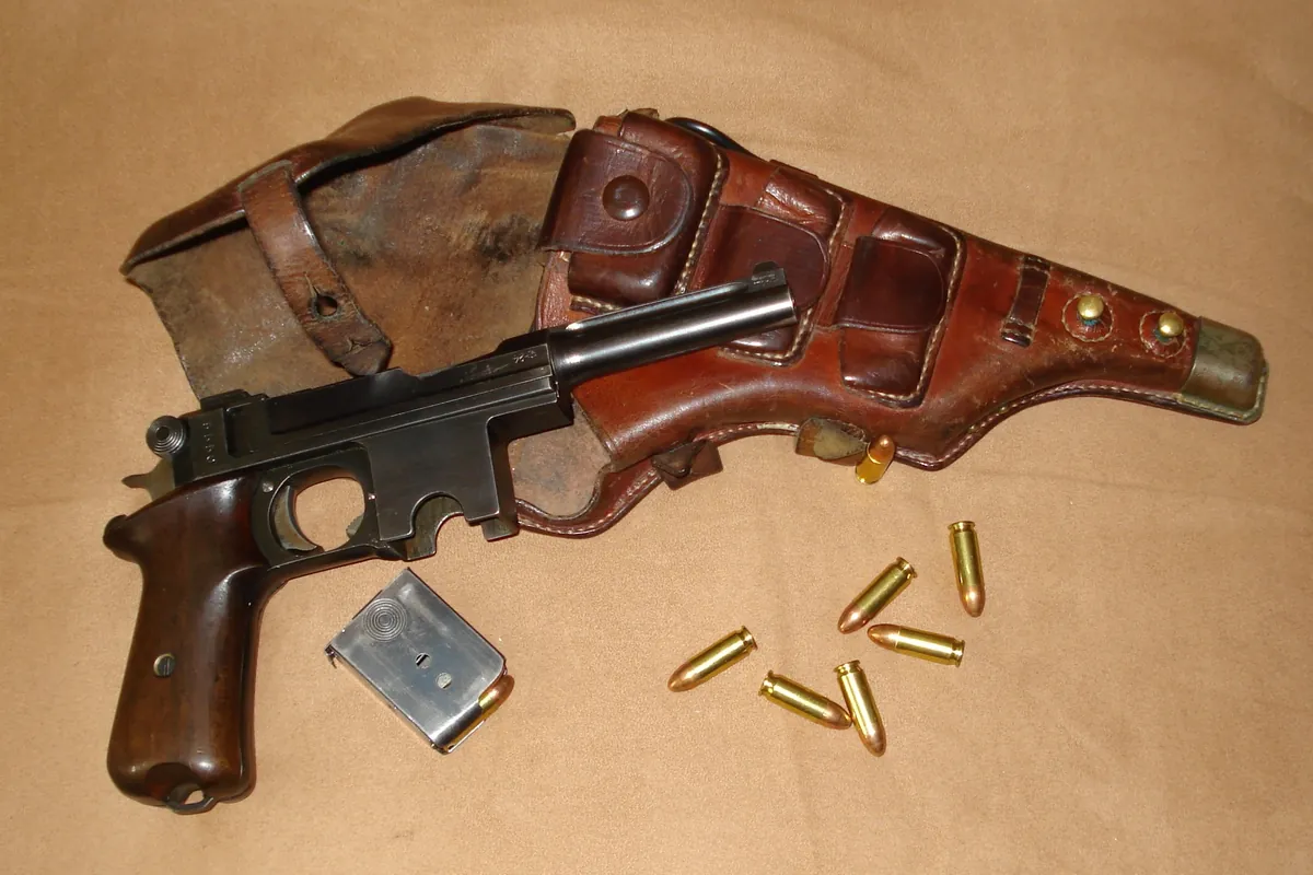 A Bergmann-Bayard pistol lying beside its brown leather military holster, a detachable box magazine and several loose cartridges