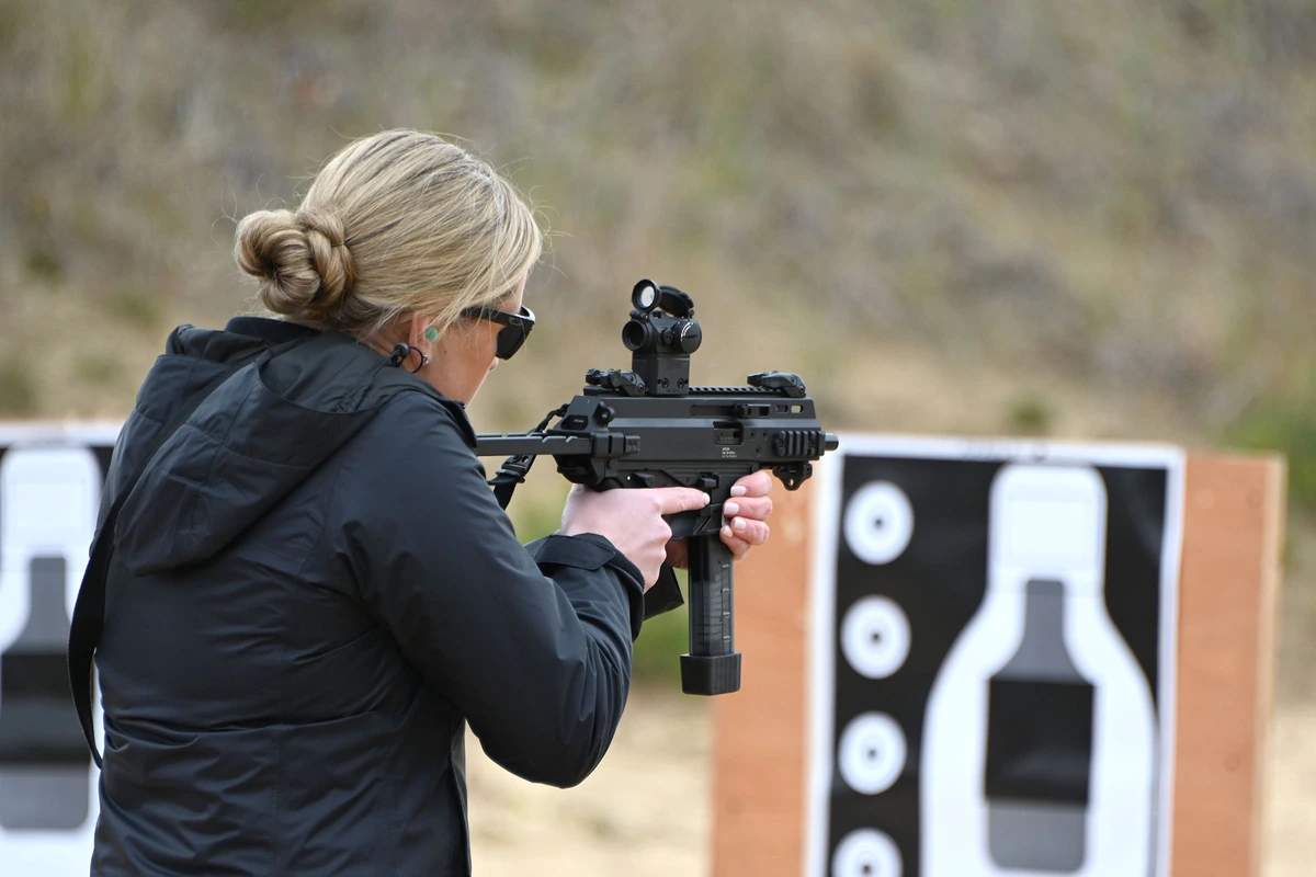 A soldier firing an APC9K submachine gun fitted with a red dot sight on an outdoor range