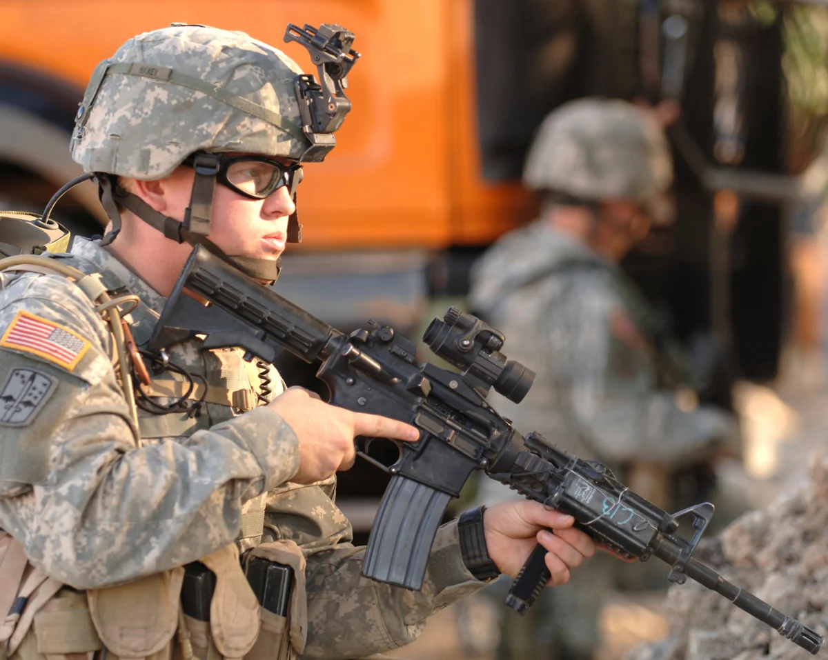 A soldier holding an M4 carbine fitted with a rail system and optic