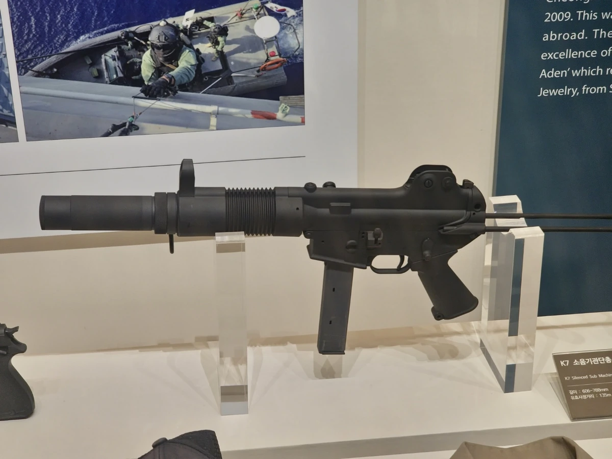 A K7 submachine gun with retractable stock extended, mounted on a museum display stand
