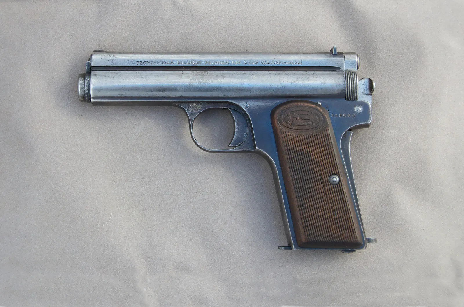 A small nickel-finished semi-automatic pistol with wooden grip panels, photographed from the left side against a plain grey background