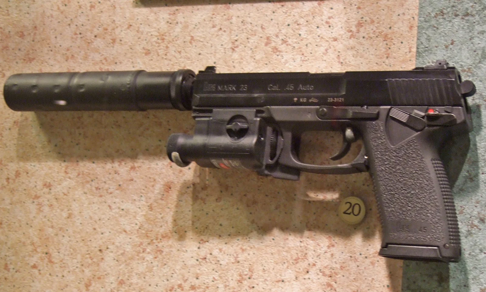 A large semi-automatic pistol with a long cylindrical suppressor threaded onto its barrel, photographed on a mottled tabletop.