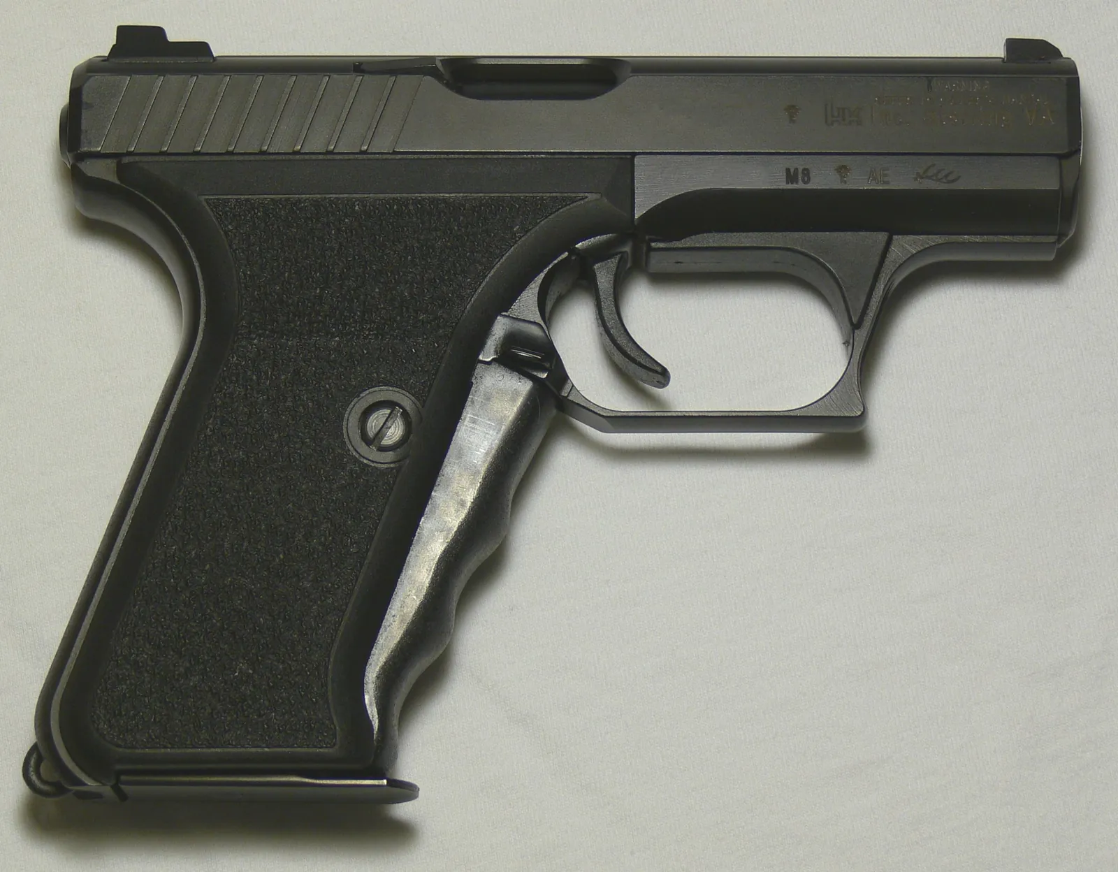 A Heckler & Koch P7M8 pistol on a pale cloth, seen from the left, with a squared black slide, stippled grip panels and a large lever running down the front of the grip