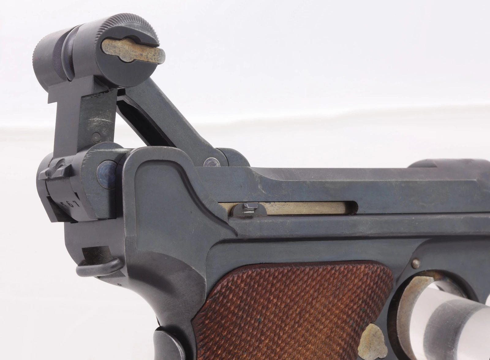A close-up of the rear of a Luger pistol against a white background, showing the toggle links raised into an inverted V above the frame, with the chequered wooden grip below
