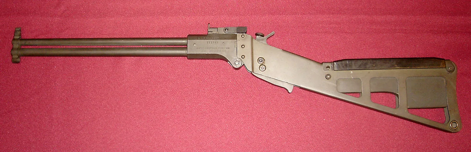 A folding stainless-steel combination gun with two stacked barrels, a skeletonized wire stock, and simple open sights