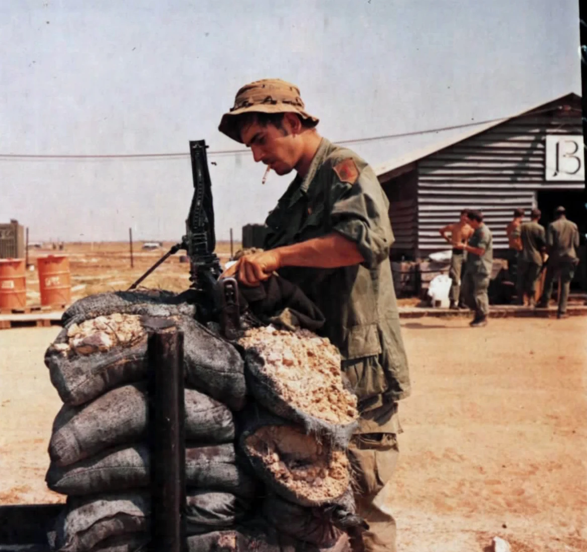 A soldier sitting on the ground field-stripping and cleaning an M60 machine gun, with its barrel and bipod disassembled beside him