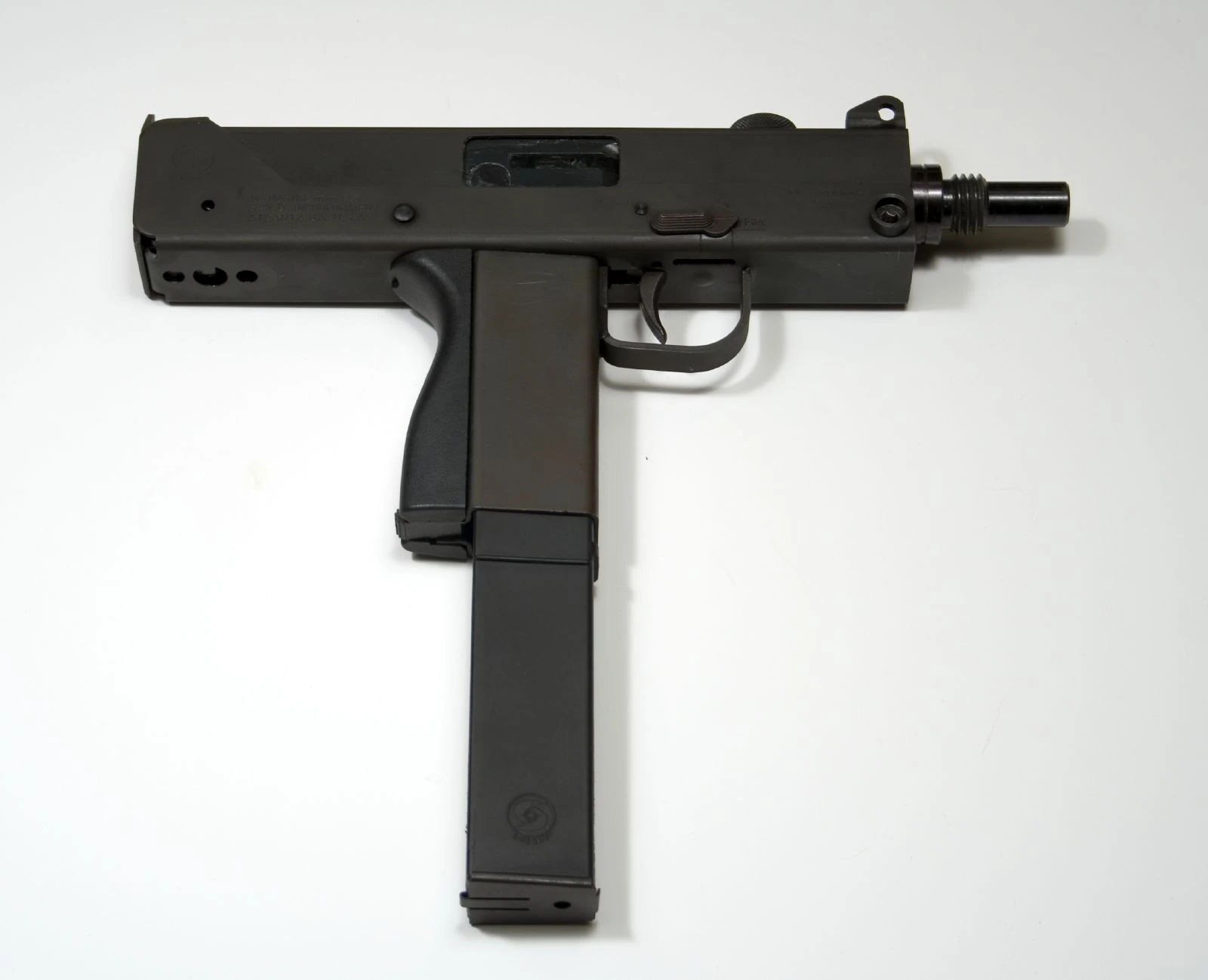 A compact black submachine gun with a stubby threaded barrel, a boxy sheet-metal receiver, a vertical pistol grip and no shoulder stock attached, its long magazine extending well below the grip.