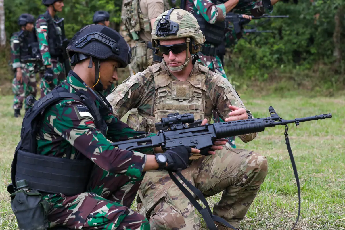 A kneeling U.S. Army soldier shows an Indonesian TNI soldier a Pindad SS2 rifle fitted with an optical sight during a joint range training exercise