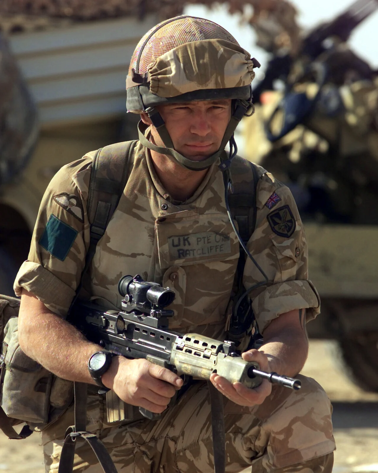 A British soldier in helmet and body armour kneeling and aiming a black bullpup rifle fitted with an optical sight, with the magazine and pistol grip set well forward of the shoulder stock