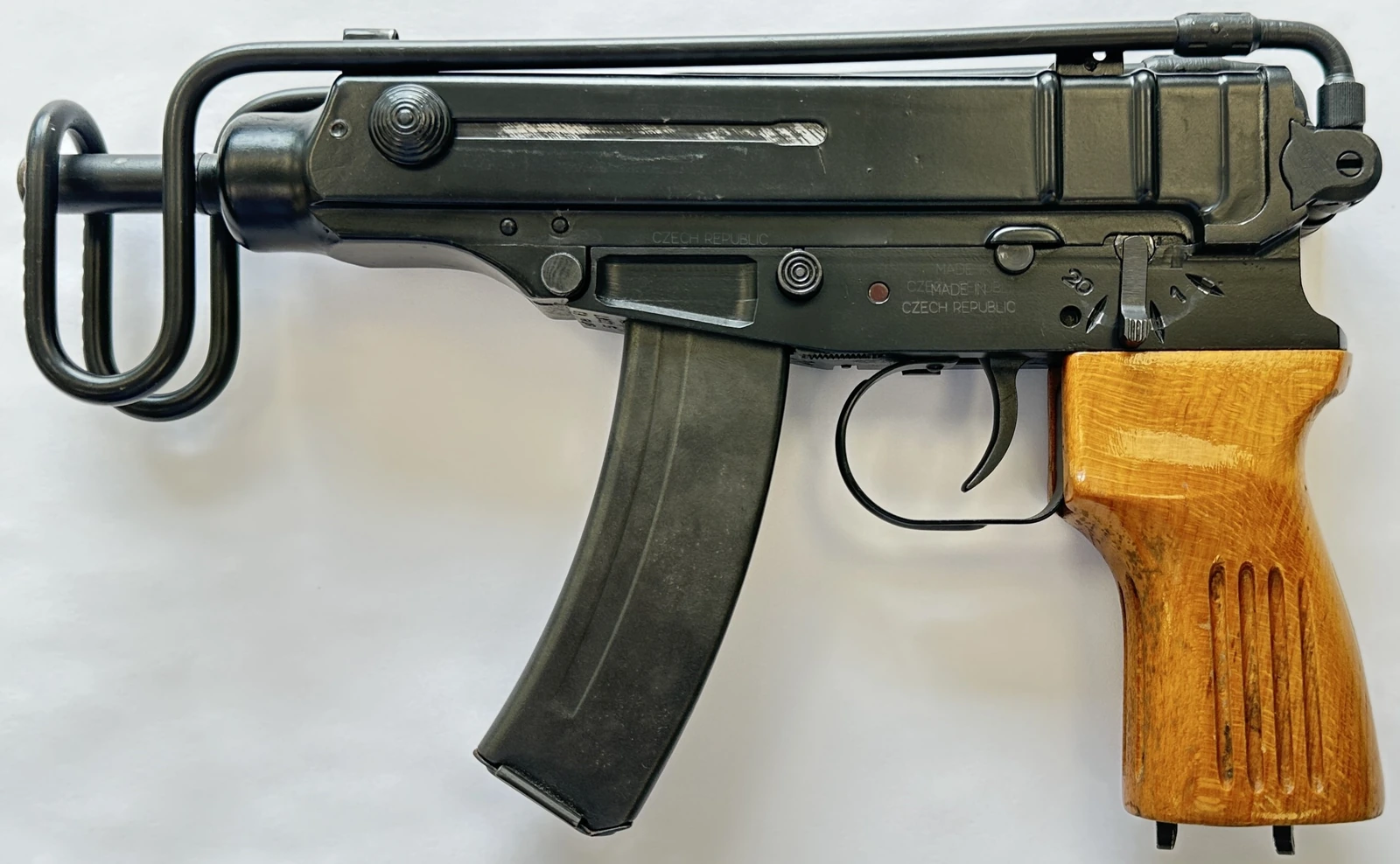 A small dark green machine pistol with a curved box magazine, a wire stock folded along the receiver, and a wooden pistol grip.