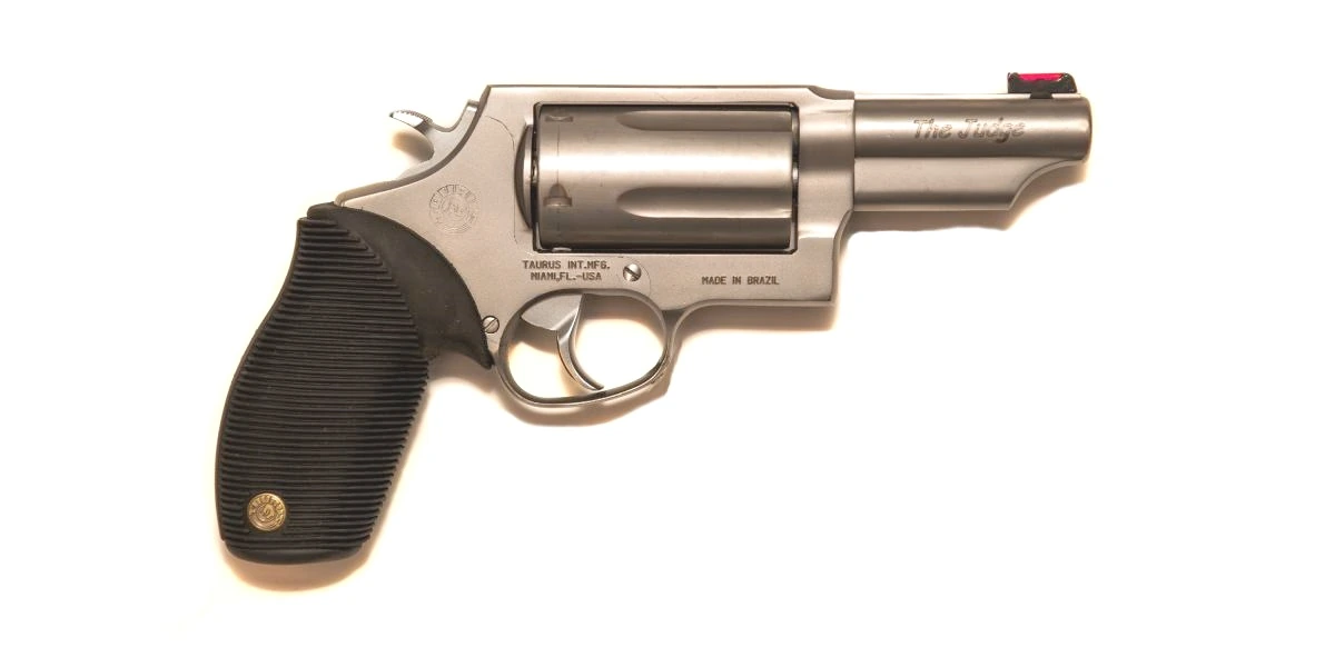 A stainless steel Taurus Judge revolver with black rubber grip, photographed against a plain ground