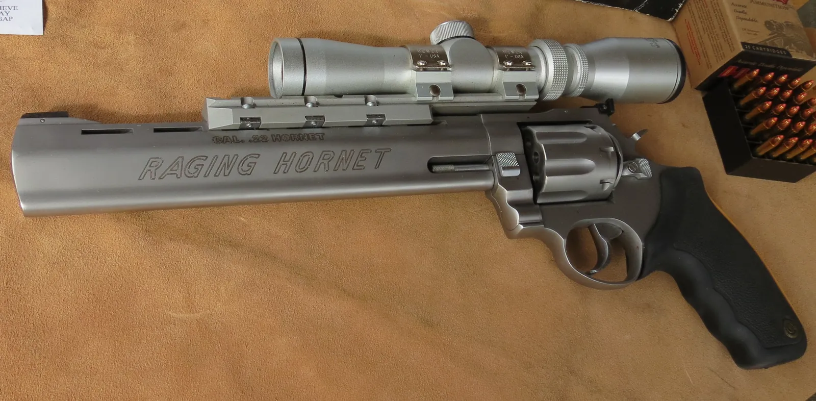 A stainless steel revolver labelled RAGING HORNET, fitted with a scope on rails above the barrel