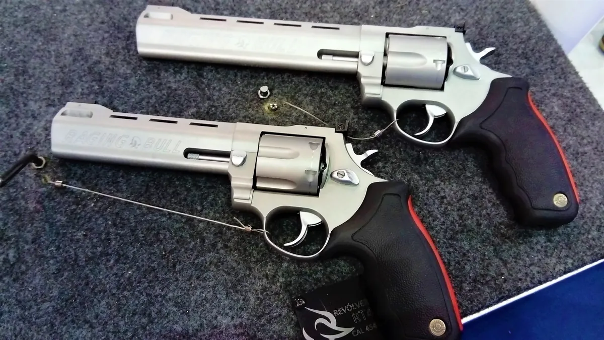 Two stainless steel Raging Bull revolvers with red-accented rubber grips, one with a longer ported barrel