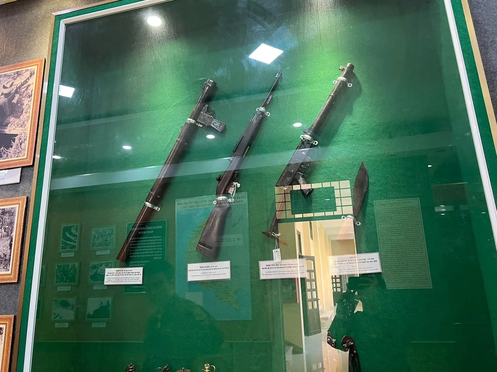 A row of four long-barreled firearms displayed behind museum glass, with a Type 64 submachine gun, its long suppressor sleeve visible, third from the left
