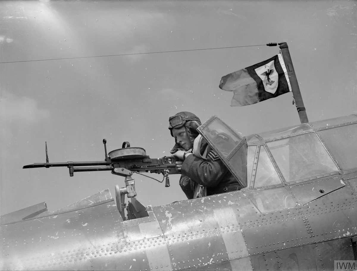 A gunner in flying gear operates a Vickers K machine gun from the open rear cockpit of a biplane bomber in flight