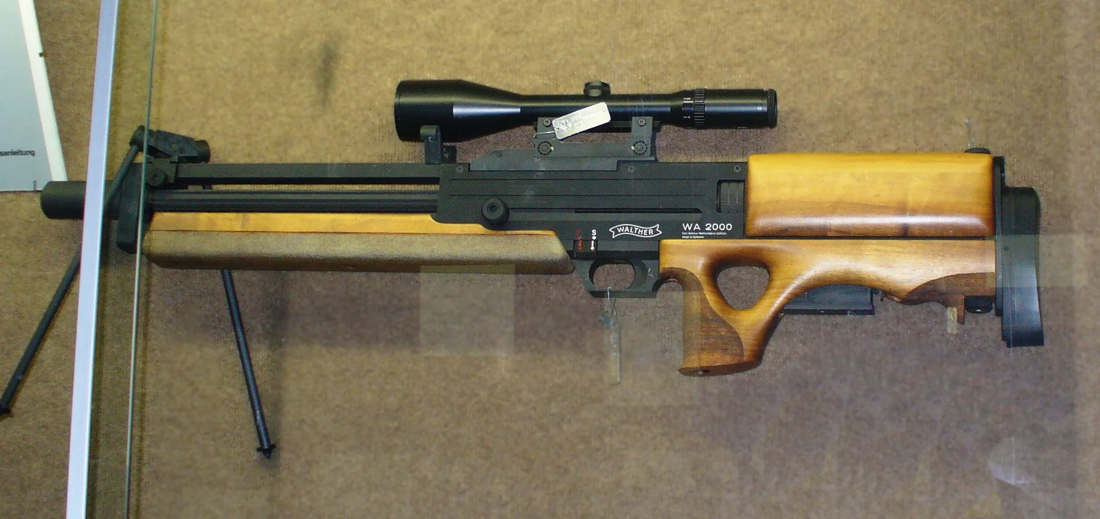 A bullpup sniper rifle with a fluted barrel and a telescopic sight, displayed in a museum case