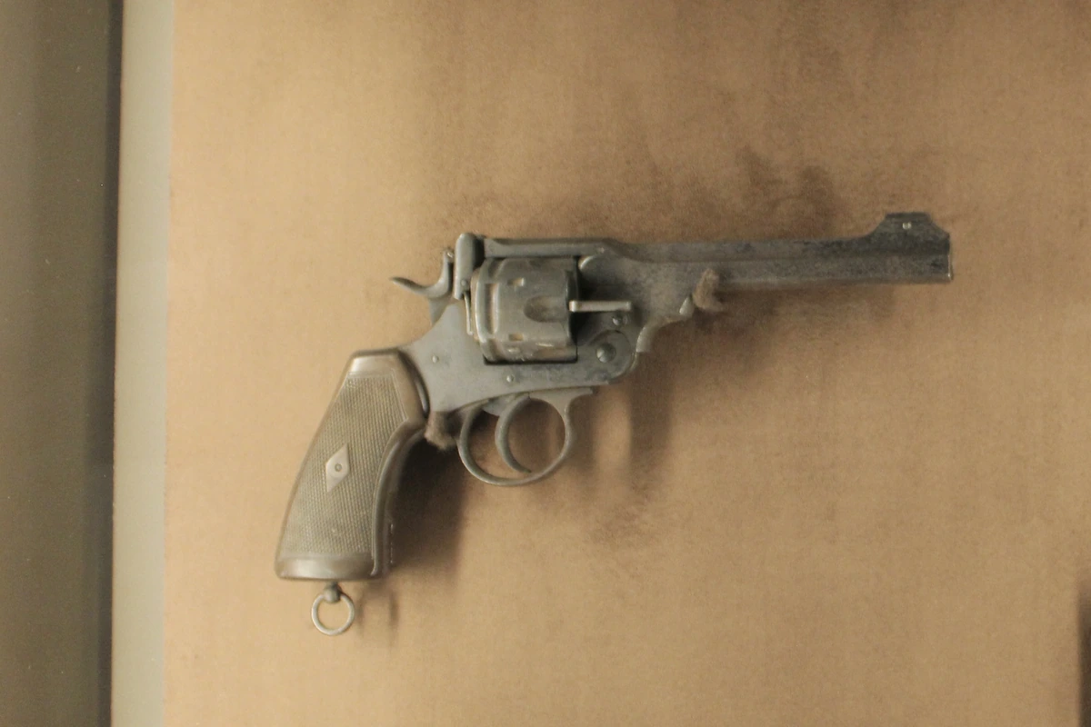A worn break-top revolver with a plain wooden grip lying against a mottled brown background.