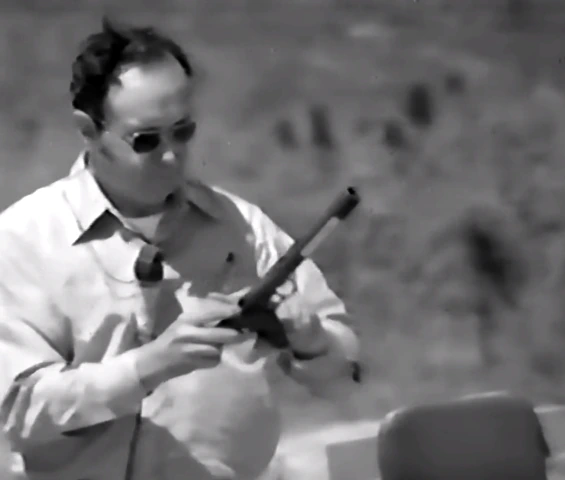 A man in civilian clothes holding a Welrod pistol during an outdoor weapons demonstration