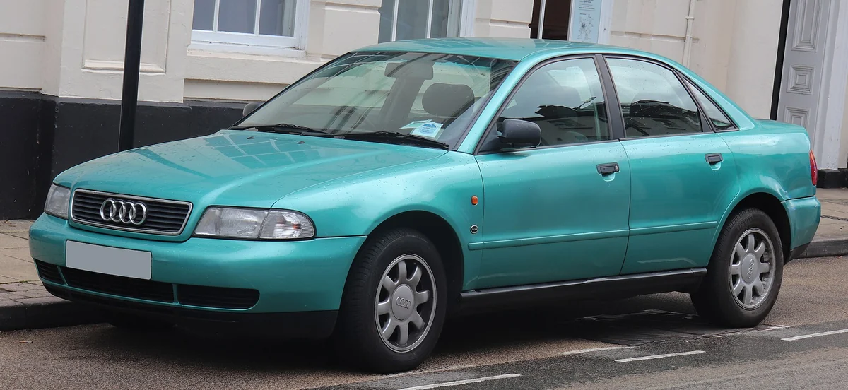 Teal Audi A4 B5 saloon photographed from the front three-quarter angle on a residential street, with a chrome single-frame grille bearing the four-rings badge