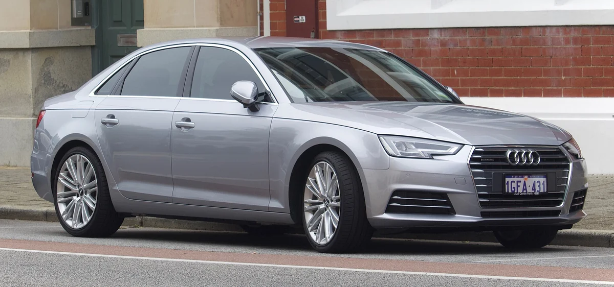 Silver Audi A4 B9 saloon photographed from the front three-quarter angle on a street, with a wide hexagonal single-frame grille and slim LED headlights