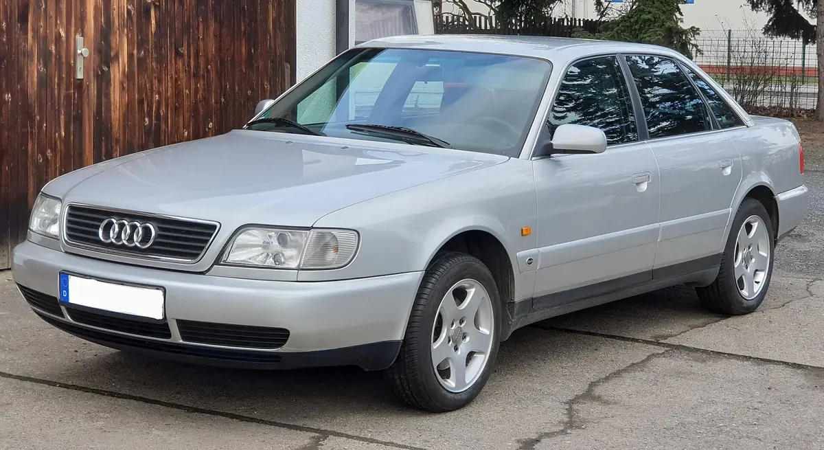 Silver Audi A6 C4 saloon photographed from the front three-quarter angle in a driveway, with a chrome single-frame grille bearing the four-rings badge
