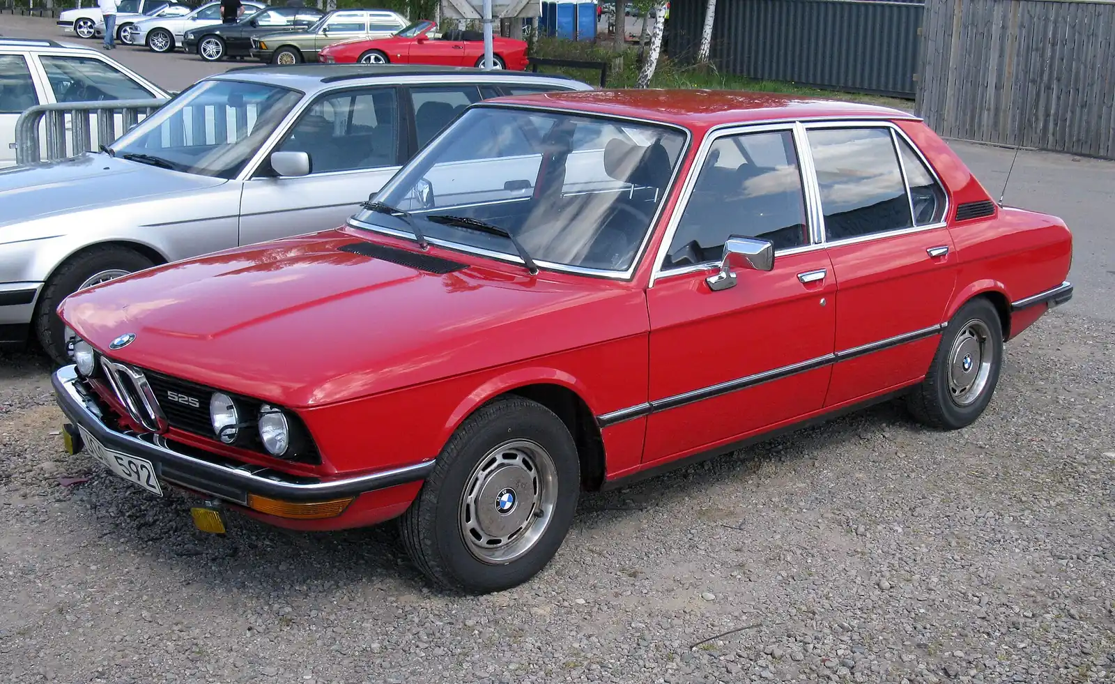 Red BMW E12 525 saloon photographed from the front three-quarter angle in a gravel car park