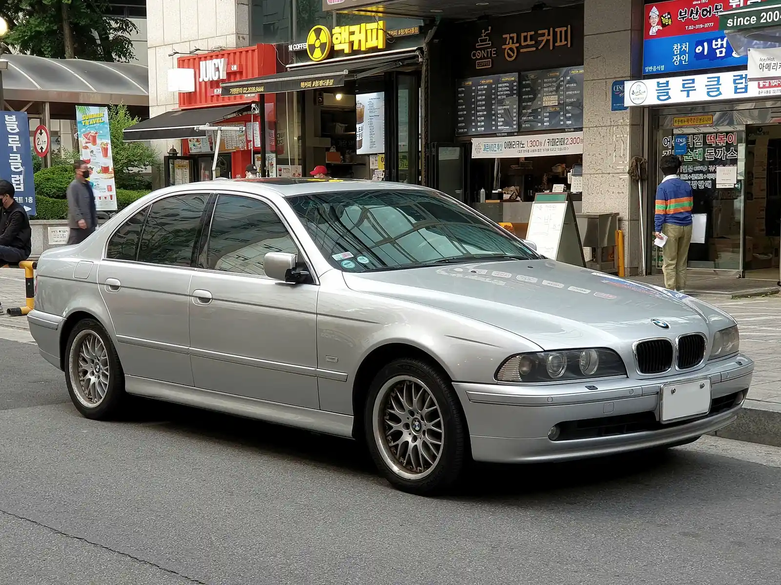 Silver facelifted BMW E39 5 Series saloon photographed from the front three-quarter angle on a city street