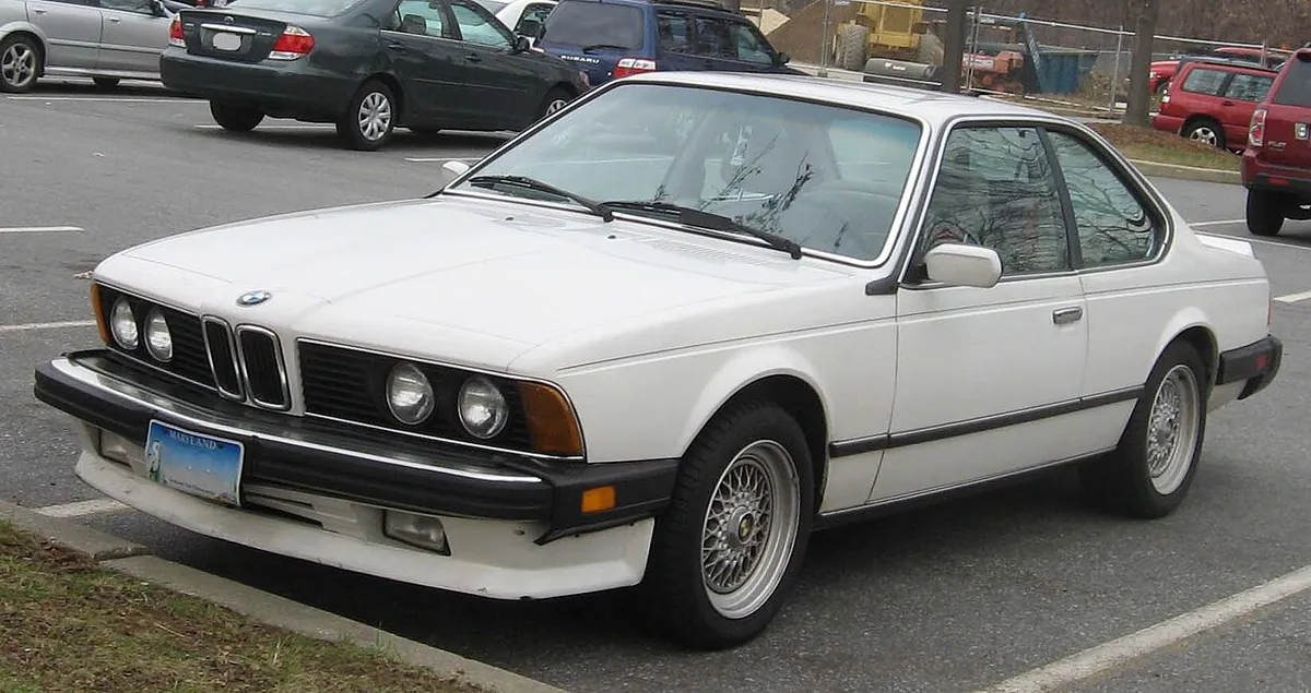 White BMW 6 Series E24 seen from the front three-quarter angle on the driver's side, in a car park