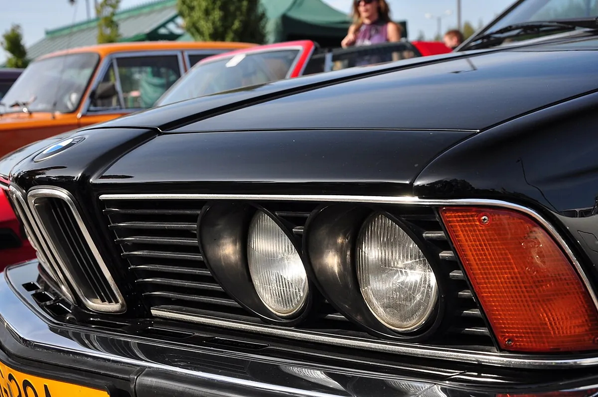 Close detail of the front of a black BMW 6 Series E24, showing the kidney grille, twin round headlamps in their recessed housings and the amber indicator lens