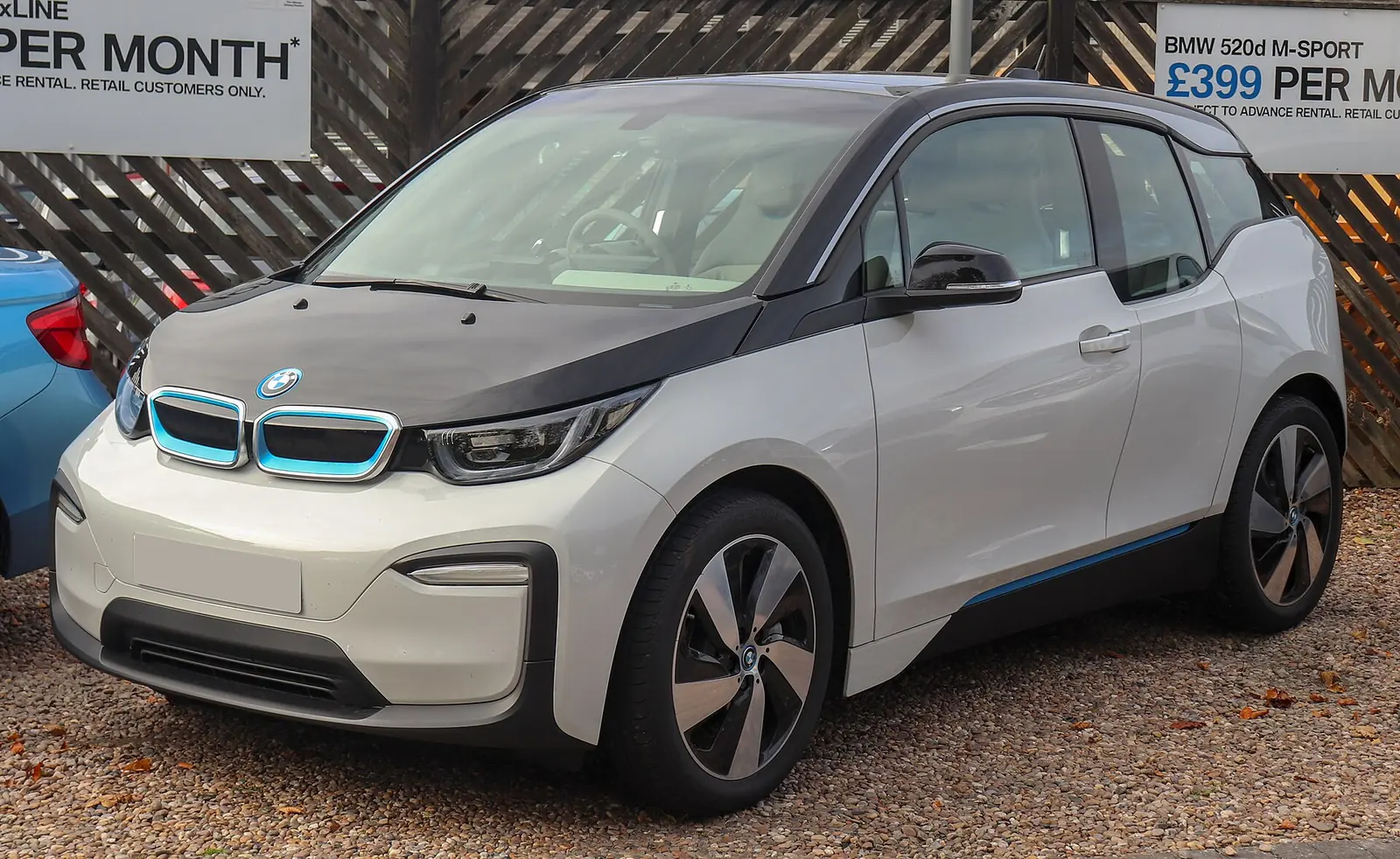 White and black two-tone BMW i3 hatchback photographed from the front three-quarter angle, parked on gravel