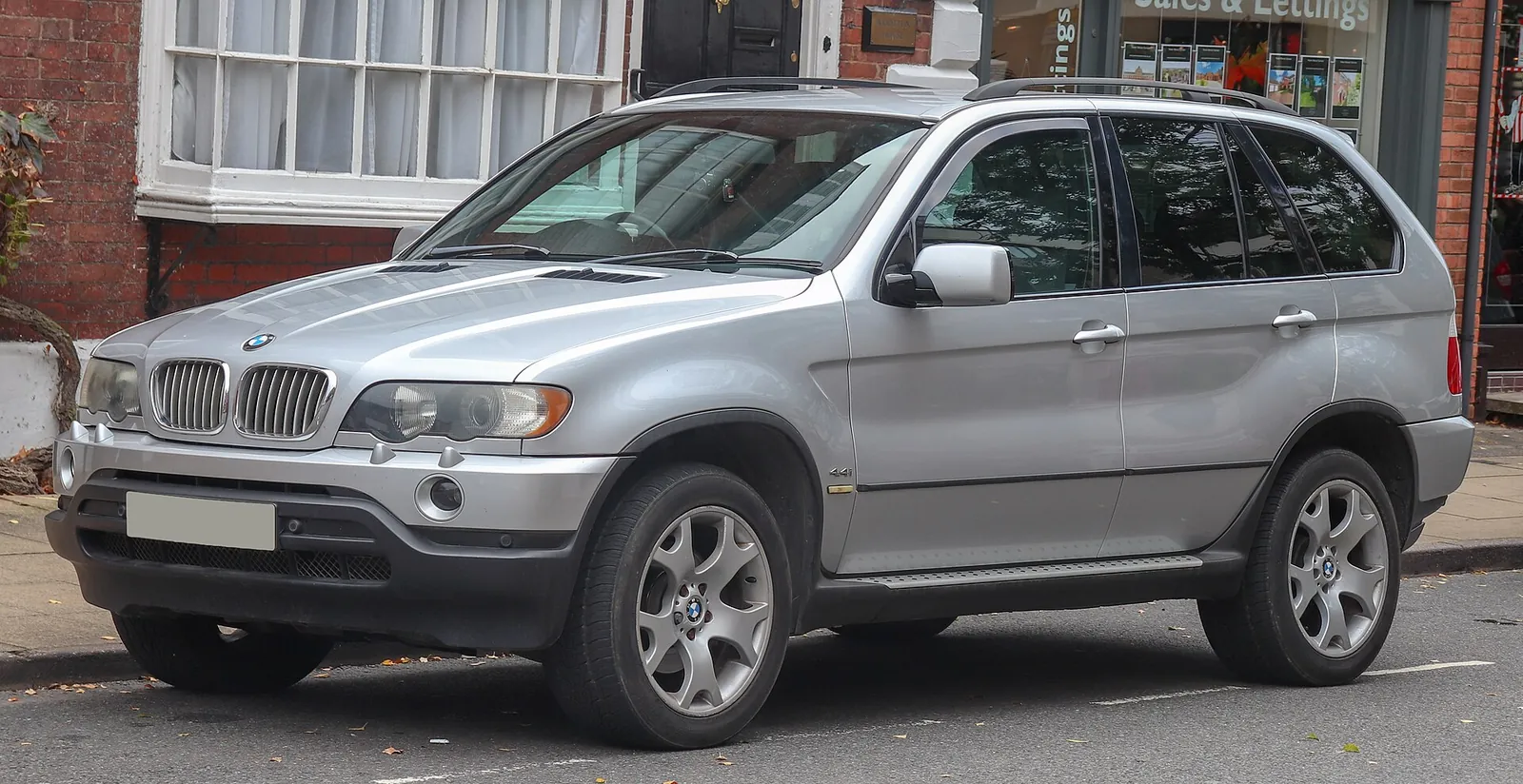 Silver first-generation BMW X5 photographed from the front three-quarter angle, showing its boxy proportions and round headlights