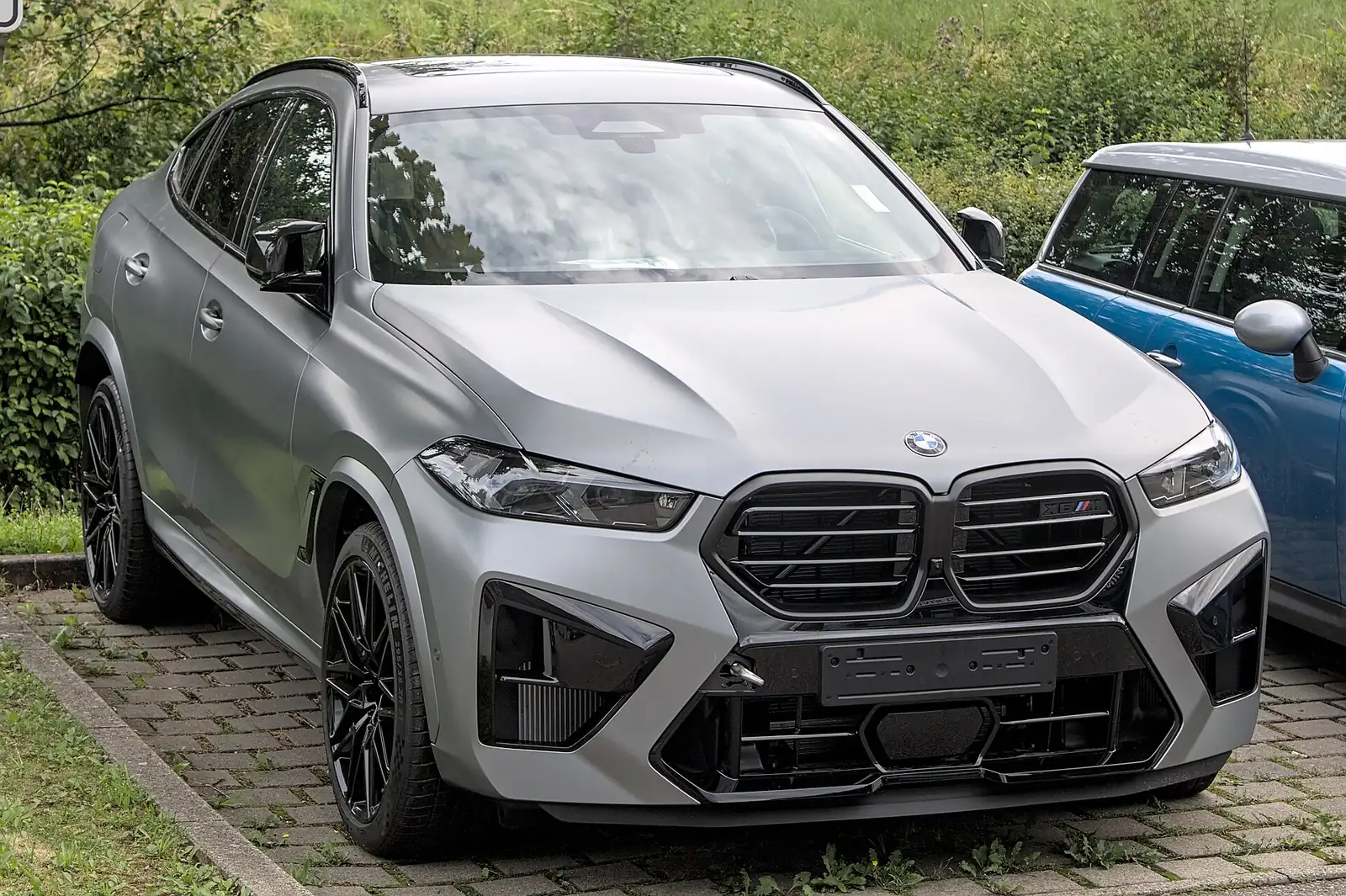 Grey BMW X6 M photographed from the front three-quarter angle, showing its large illuminated kidney grille