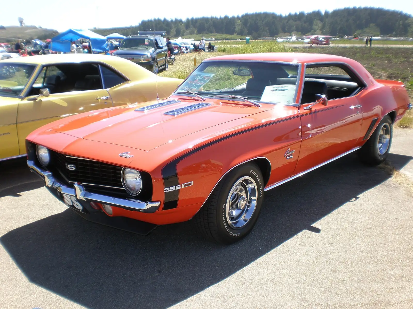 Orange 1969 Chevrolet Camaro SS 396 photographed from the front three-quarter angle at a car show, showing its black bonnet stripes and SS badging