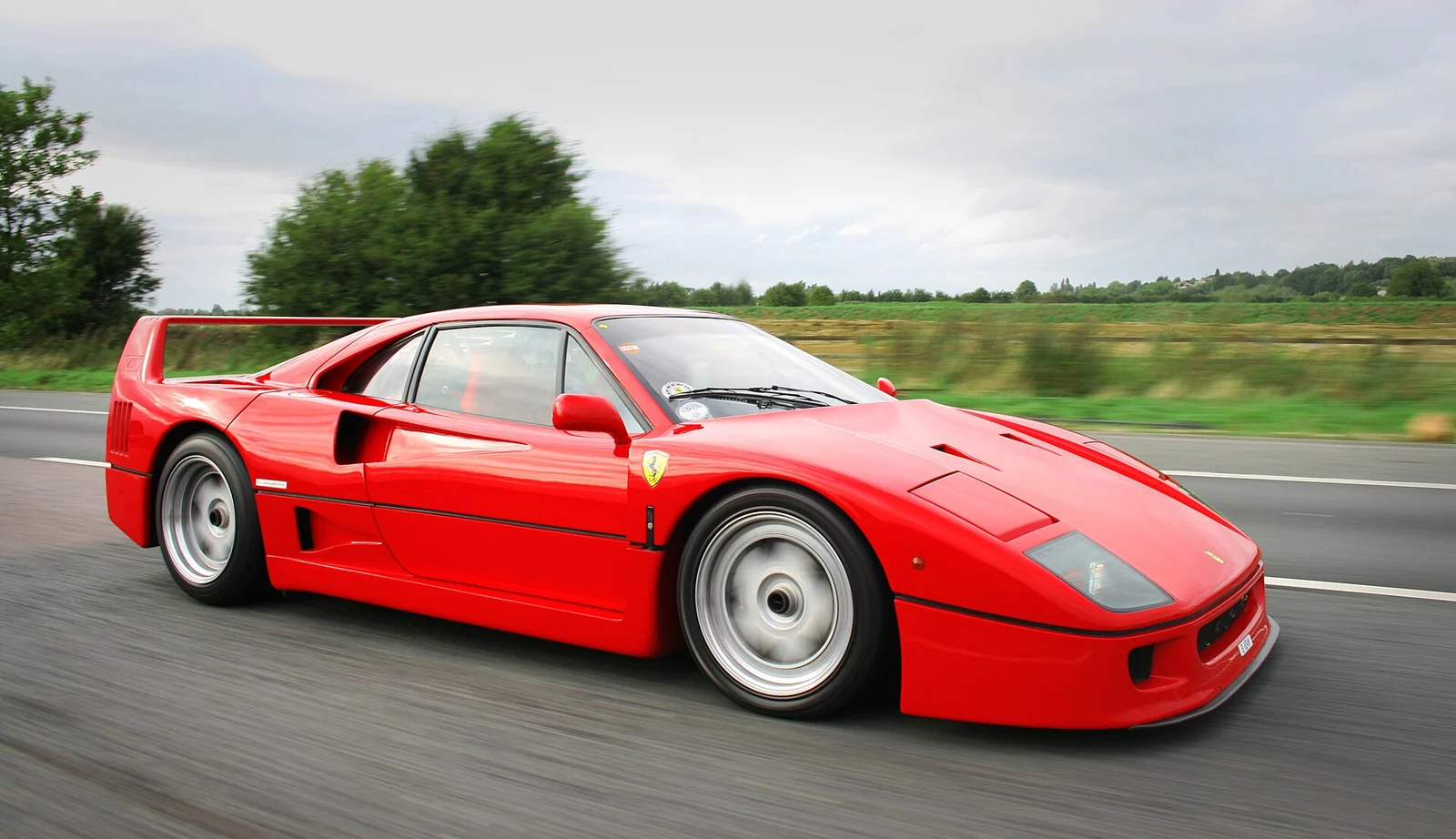 Red Ferrari F40 photographed in motion from the front three-quarter angle, showing its large rear wing and pop-up headlights