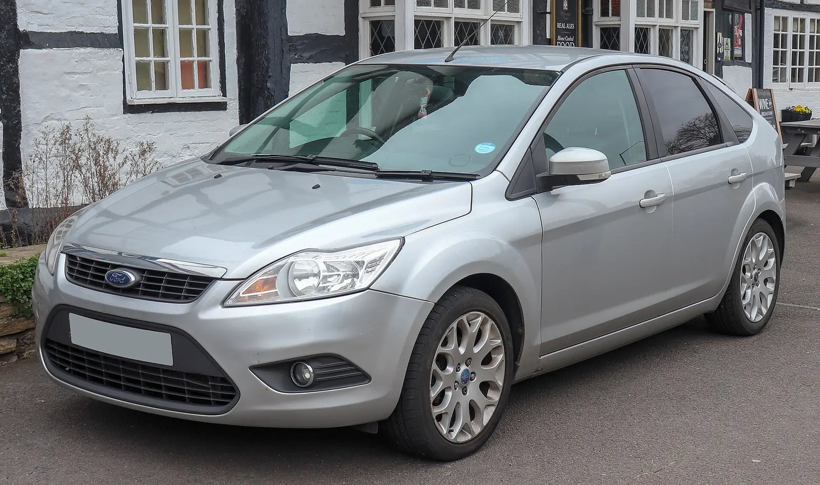 Silver facelifted second-generation Ford Focus hatchback photographed from the front three-quarter angle outside a pub