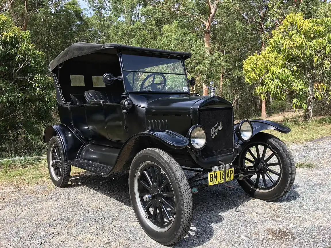A 1925 Ford Model T Touring car in dark green, photographed from the front three-quarter angle with its canvas top raised, brass-trimmed radiator shell and wood-spoke wheels on balloon tyres