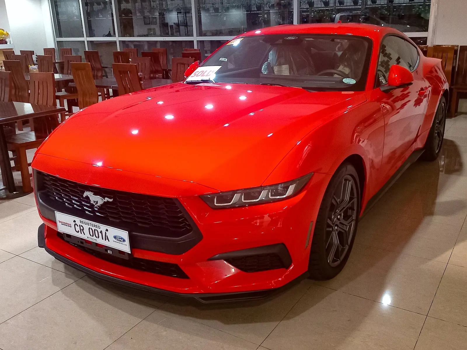 Red 2024 Ford Mustang EcoBoost coupe photographed from the front three-quarter angle in a showroom