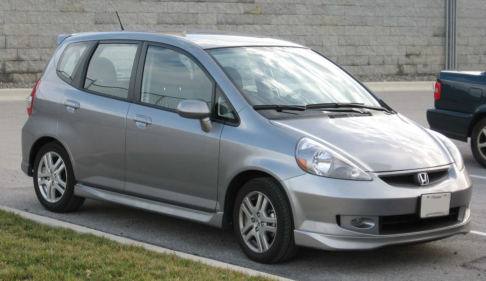 Silver first-generation Honda Fit Sport photographed from the front three-quarter angle, showing its tall, short-nosed hatchback body