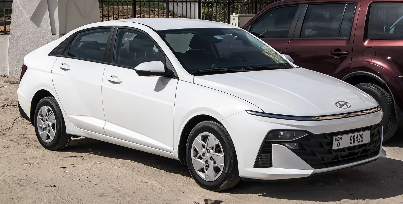 White sixth-generation Hyundai Accent saloon photographed from the front three-quarter angle, showing the connected LED light bar and sharp-edged bumper