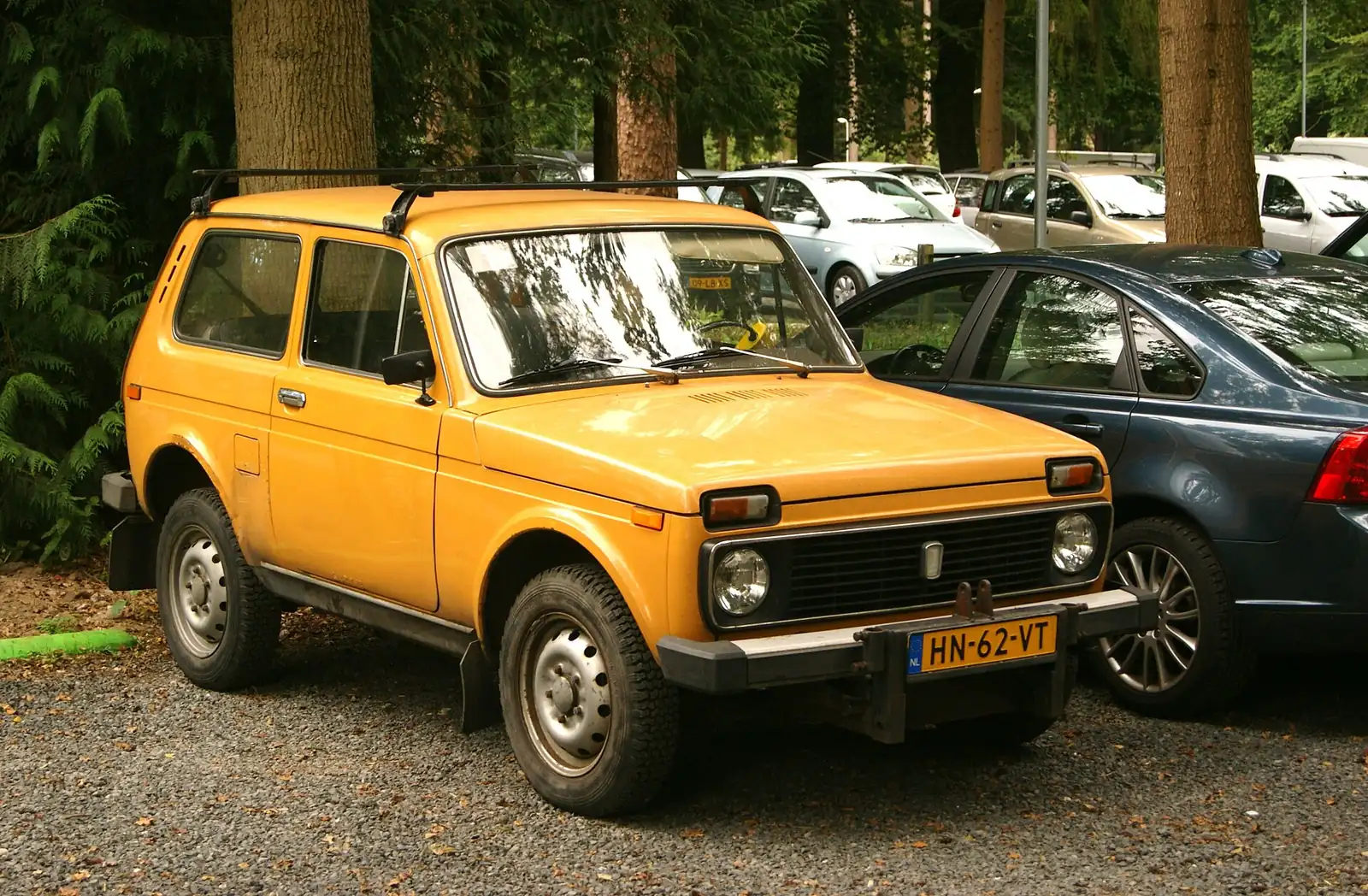 Yellow original Lada Niva photographed from the front three-quarter angle in a car park, showing its boxy body and round headlights