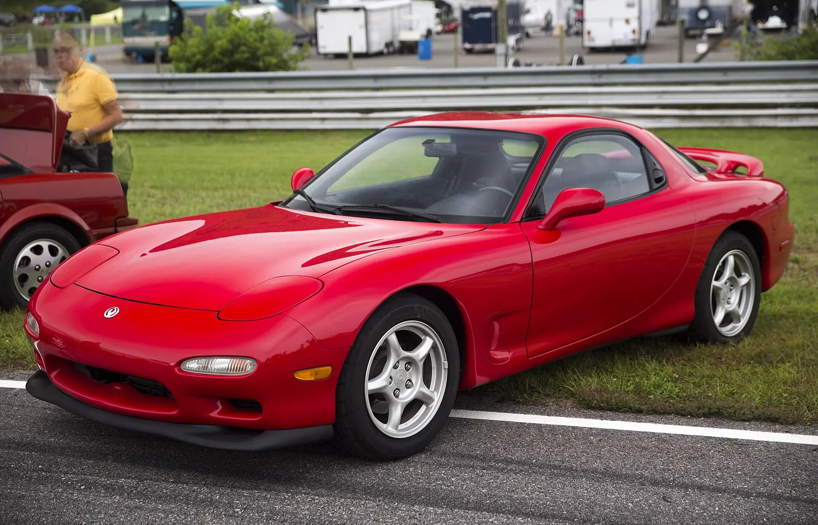 Red third-generation Mazda RX-7 photographed from the front three-quarter angle on a racetrack, showing its smooth pop-up-headlight nose and rounded flanks