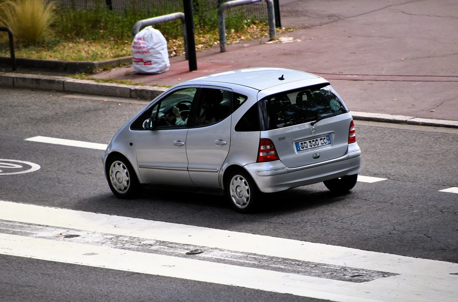 Silver first-generation Mercedes-Benz A-Class hatchback photographed from the rear three-quarter angle while driving on a city street