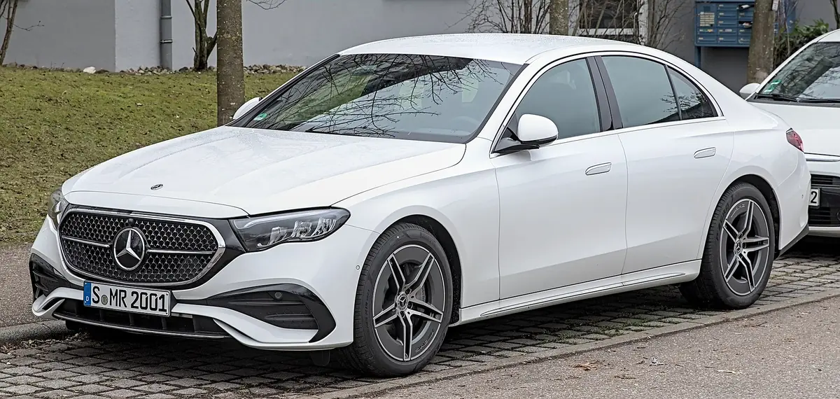 White Mercedes-Benz E-Class W214 saloon photographed from the front three-quarter angle on a residential street, with a diamond-pattern grille bearing a large central star